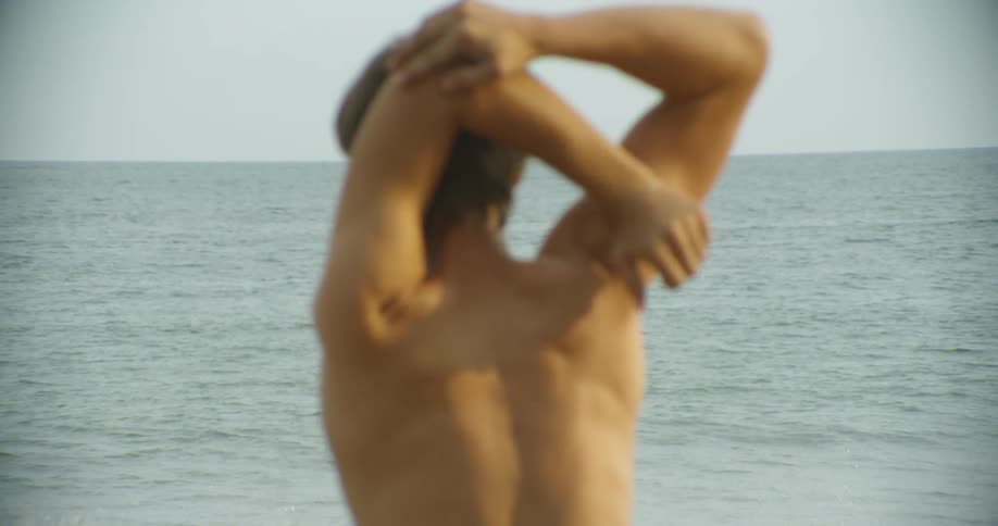 Man stretches his arms as he looks out at the water