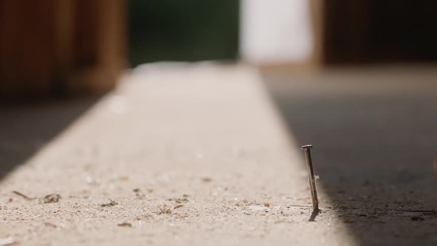 A person holds a long nail steady and then hammers it in