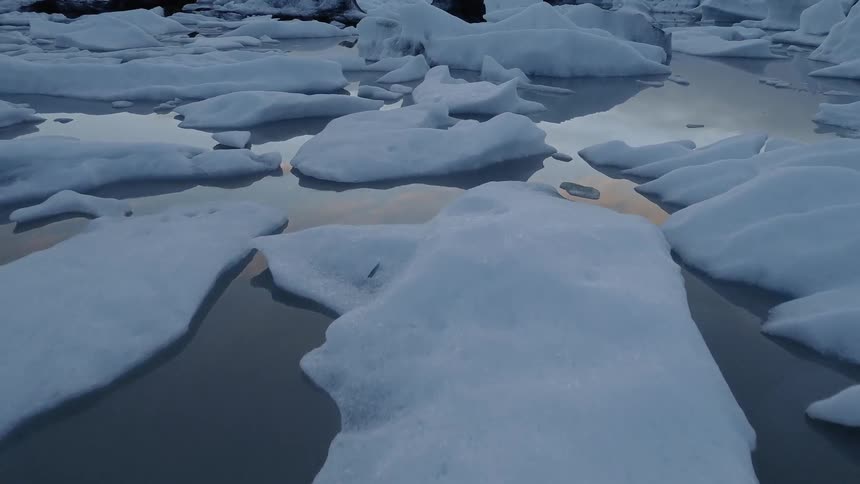 Snow and ice float on a lake at sunset