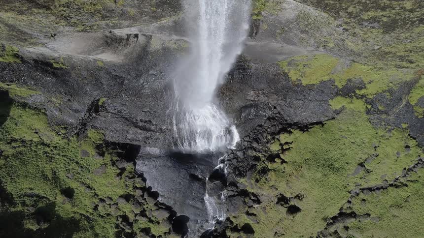 A waterfall flows over a mossy cliff