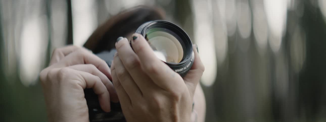 Woman stands outside in the woods taking pictures