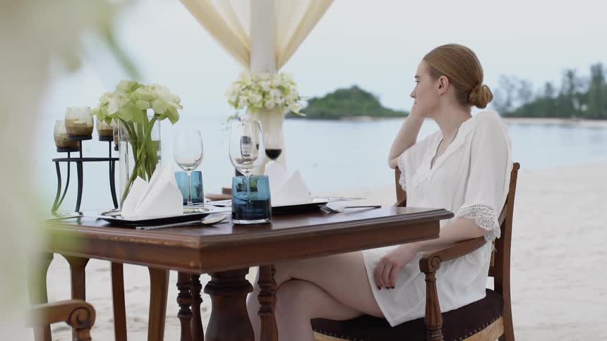 A woman sits at a table set for two overlooking the ocean