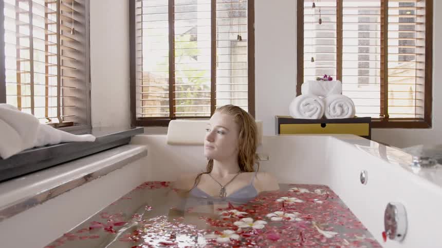 Woman sits in a tub of water as flowers float around her
