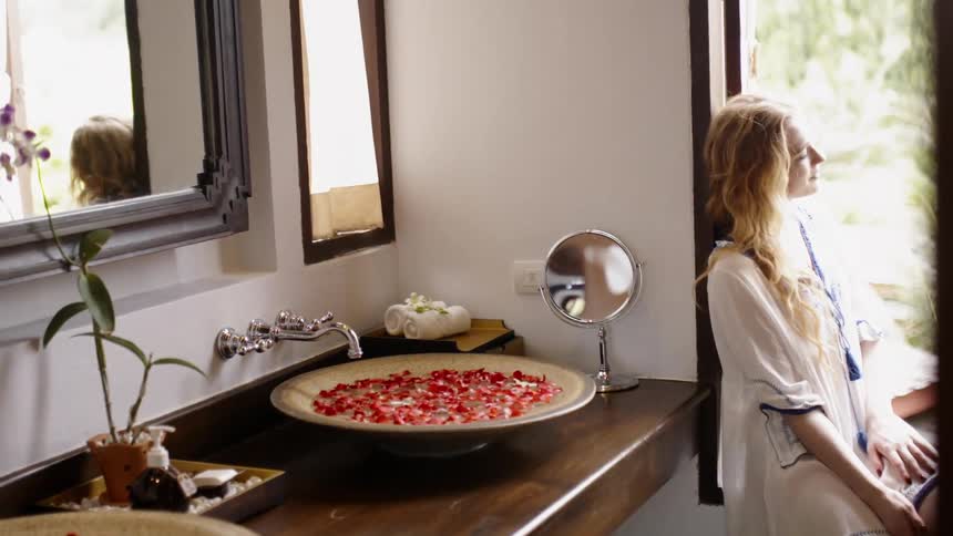 A woman sits in a bathroom with a sink full of flower petals