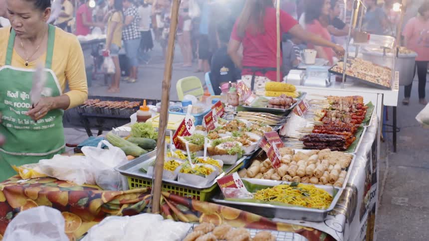 A woman fans the smoke away from the food displayed at the market