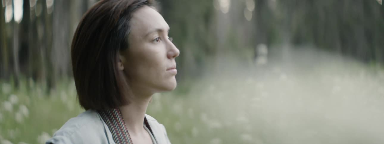 Woman pushes her hair back as she sits in a field and takes a photo