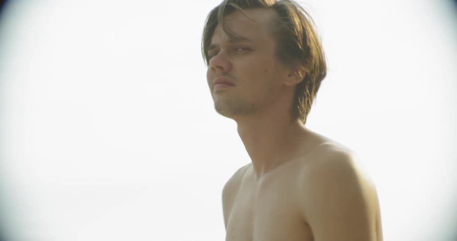 A shirtless man stands outside on a sunny day