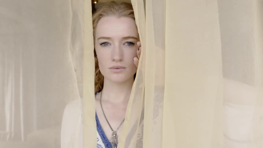 Woman is looking out a window through yellow curtain