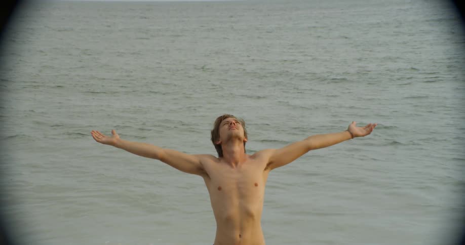 Man holds his arms up and large body of water splashes behind him