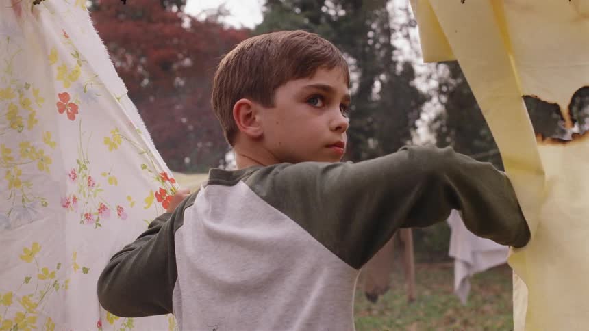 Young boy holds some fabric as he looks behind him