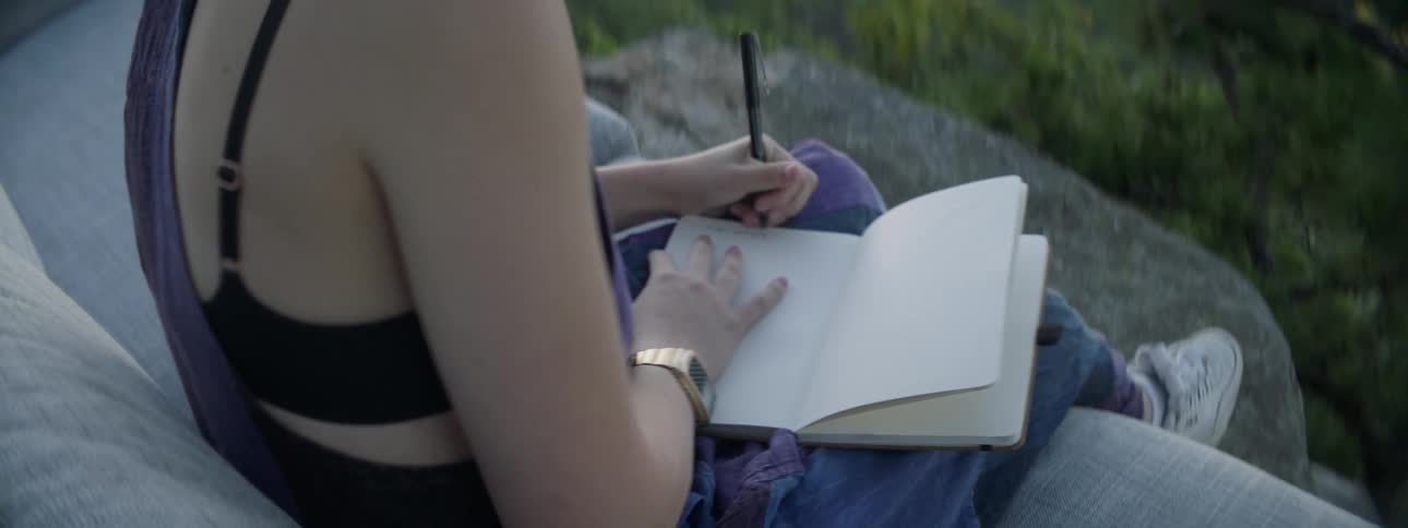 The woman is writing in the small notebook