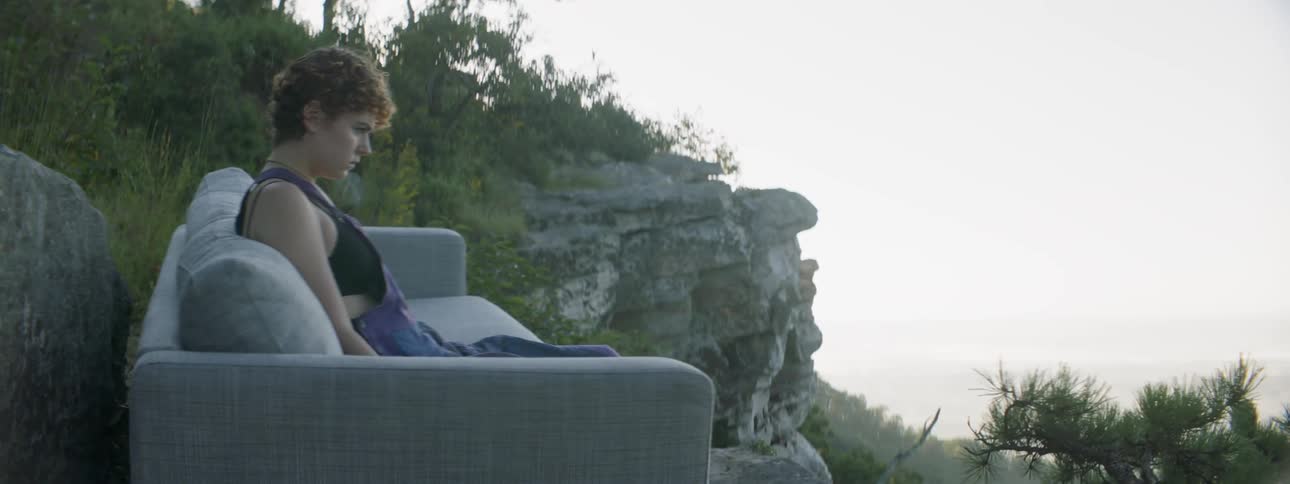 A woman sits back on a couch outside on a ridge