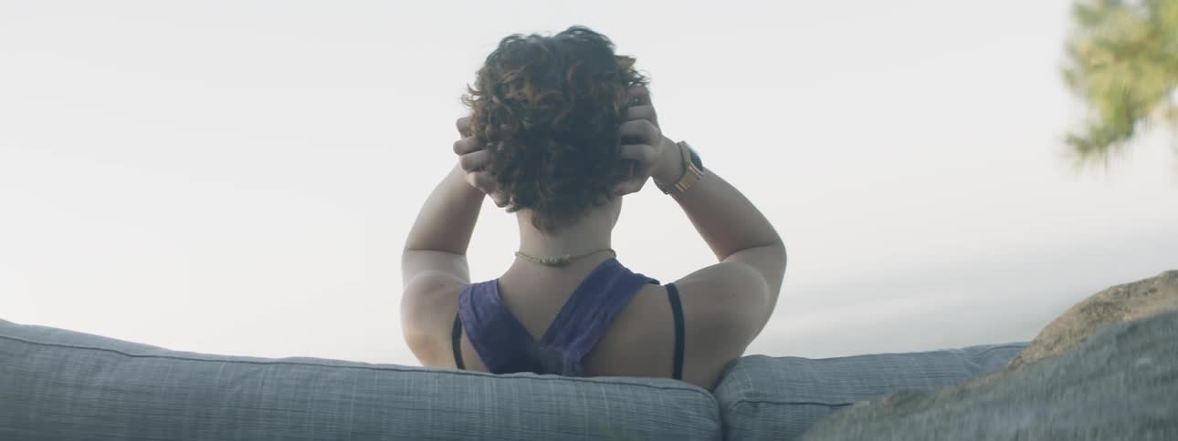 Woman grabs her hair as she sits on a cushioned sofa