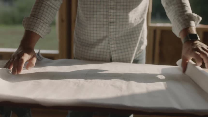 A man is unrolling a blueprint inside a construction project in daylight