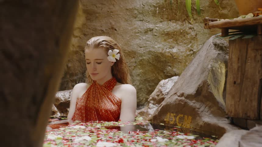 A woman sits in an outdoor spa bath with flower petals