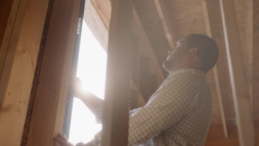 Man does some measuring around a window as the sun shines brightly