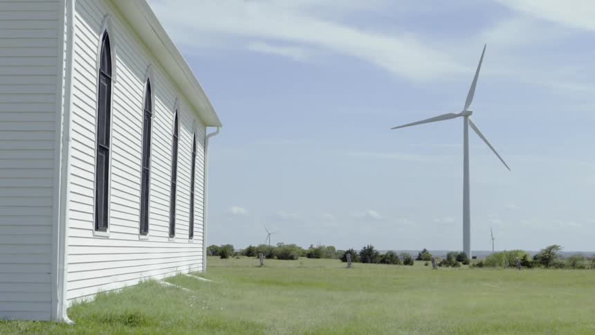 A wind turbine turns in the field near a white building