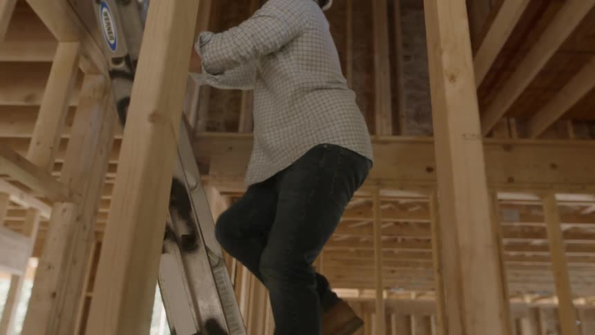 Man in a safety hat climbs a ladder in a building under construction