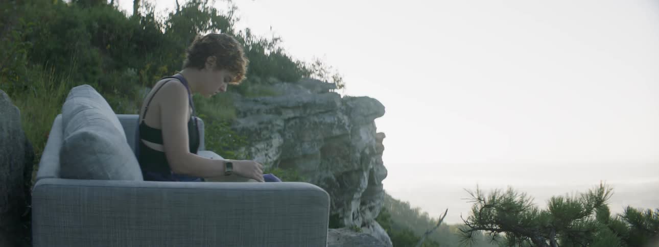 A woman reads a book on a sofa in mountains