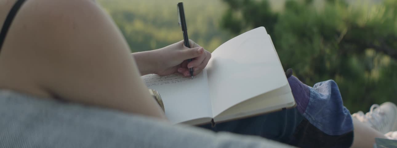A woman journals on a sofa outside