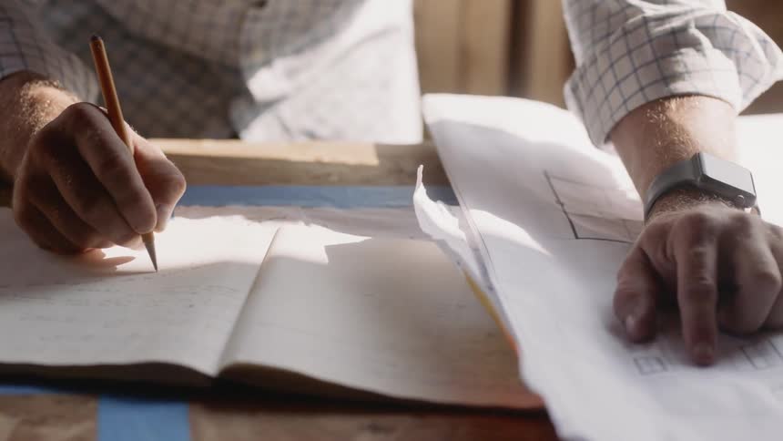 A man writes in a notebook while looking at floor plans