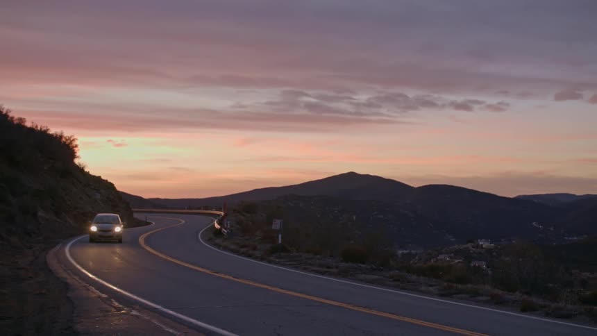A car driving down a winding mountain road during sunset
