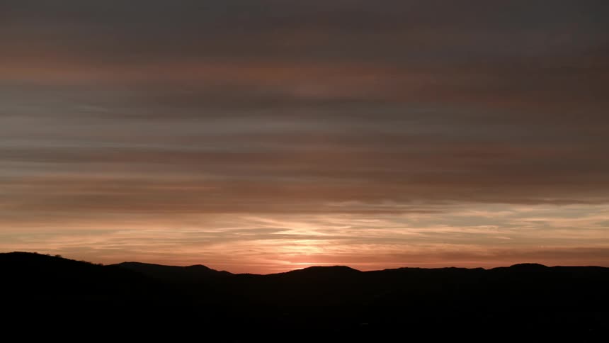 Sunset behind a cloudy sky on the hilly horizon