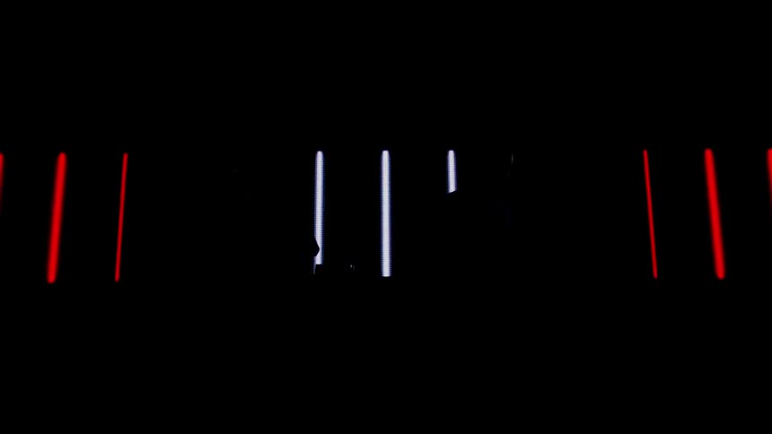 Two men move in front of an illuminated screen