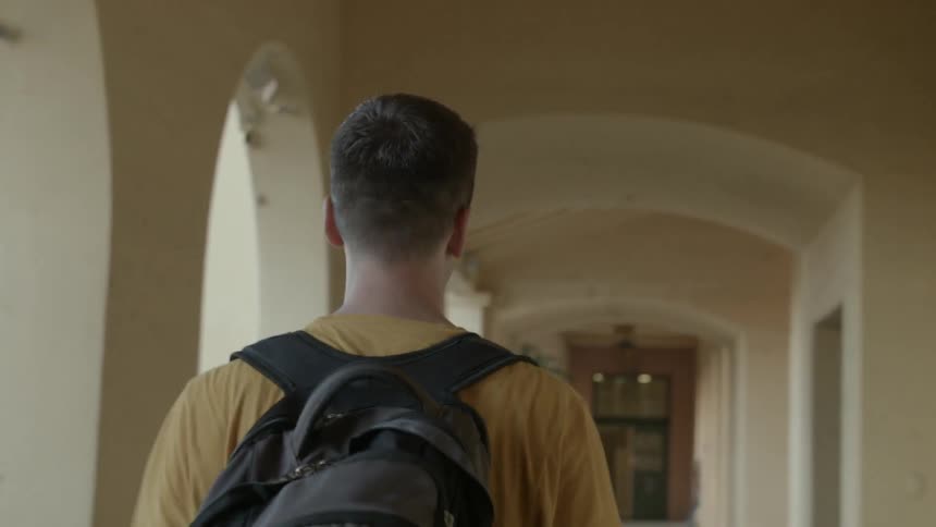 A man with a backpack walks on the porch of a building