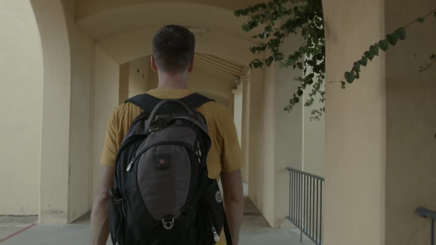 A man with a backpack walks on the porch of a building