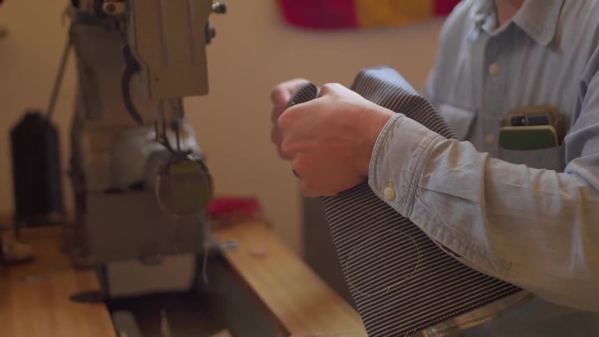 A man is sewing material on a sewing machine during daylight