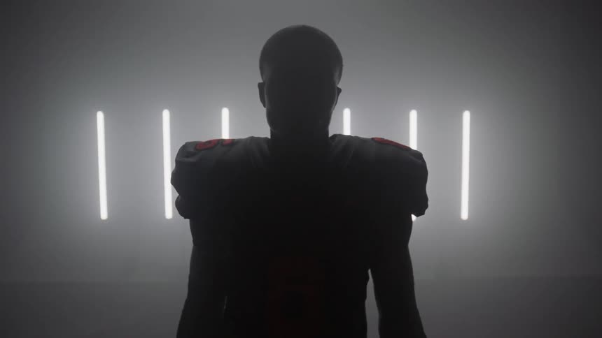 A football player stands in a room with strip lights