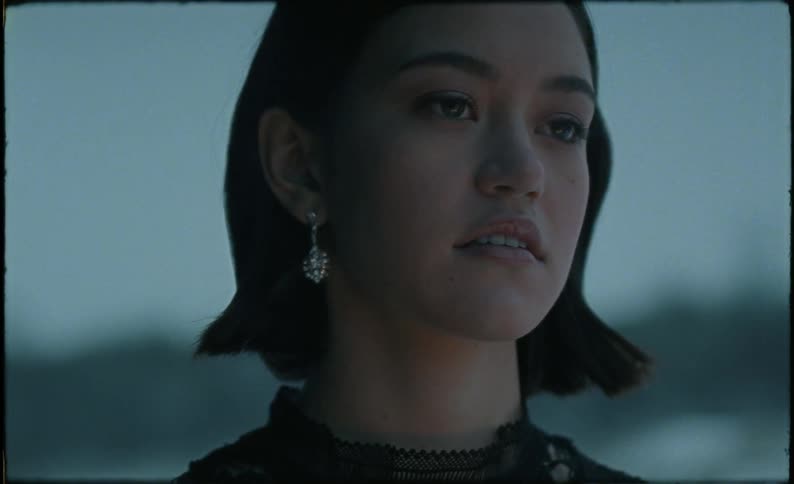 A woman stands outside in the snow and the light of a fire shines on her face