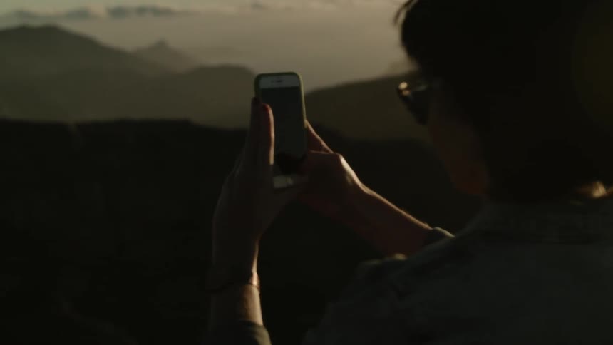 Woman wearing sunglasses holding up her phone at sunset