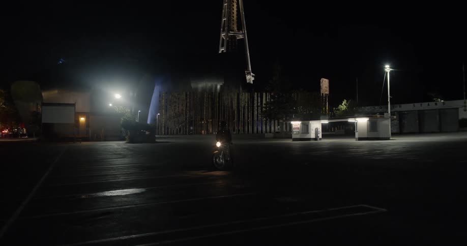 A motorcyclist is stopped in a parking lot at night