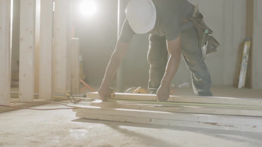 Man in hard hat is measuring piece of wood at construction site