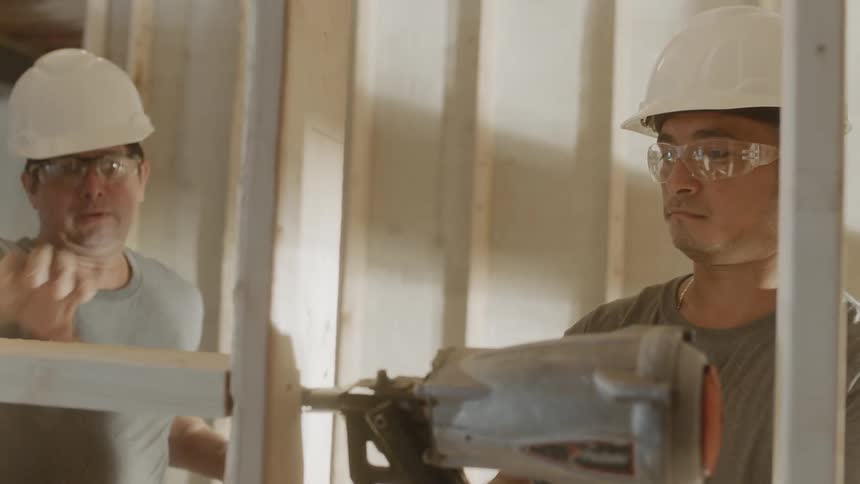 A builder uses a nail gun on wood framing