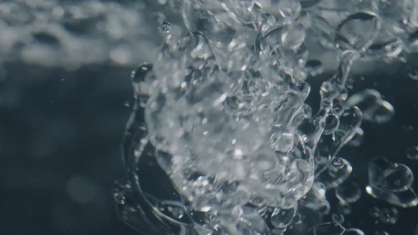 A clear liquid is falling into water and rising to the top