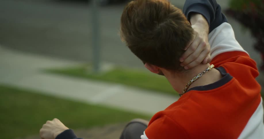 A man is sitting outside rubbing the back of his neck in daylight