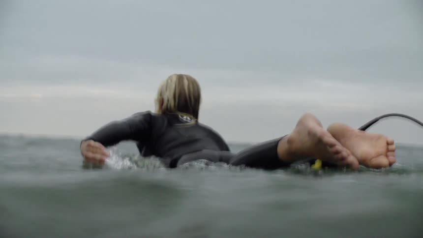 Person lays on a board in the ocean paddling with their arms
