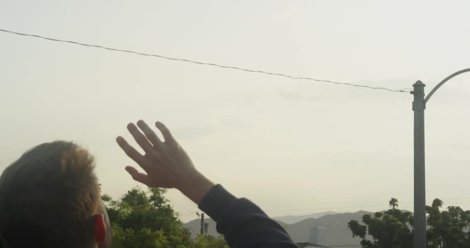 Man is smoking cigarette and watching airplane fly in the overcast sky