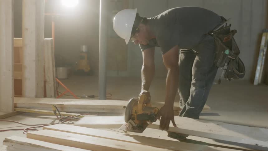 A construction worker cuts lumber with a saw