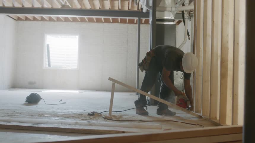 Man wearing a hard hat cuts a piece of wood