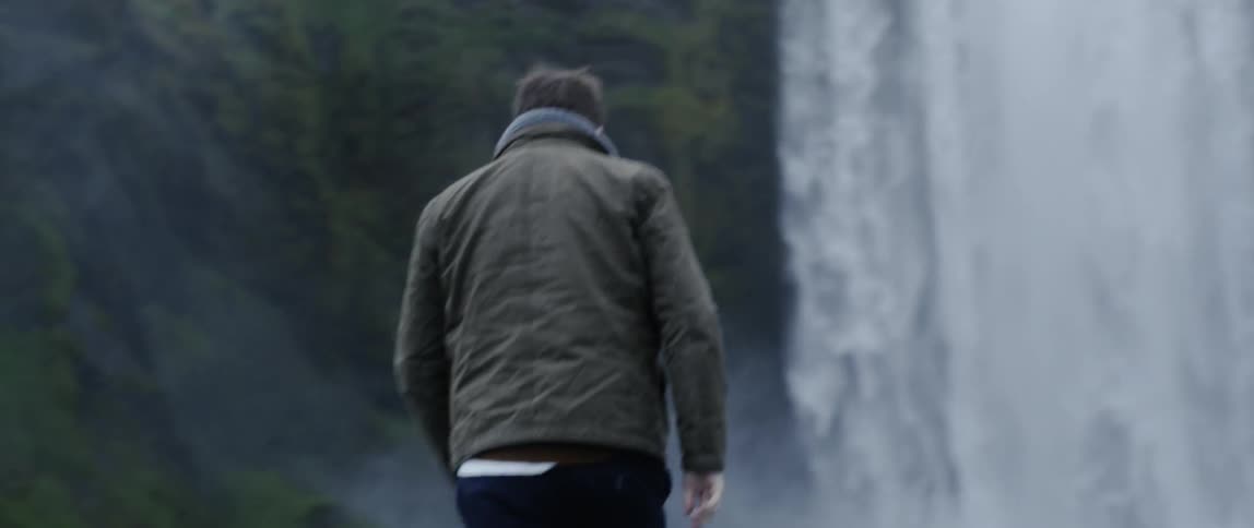 A man walks over to a large waterfall