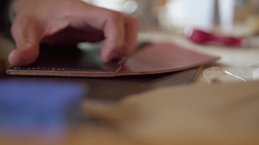 A man uses a wooden hand tool to smooth a stitched edge on leather