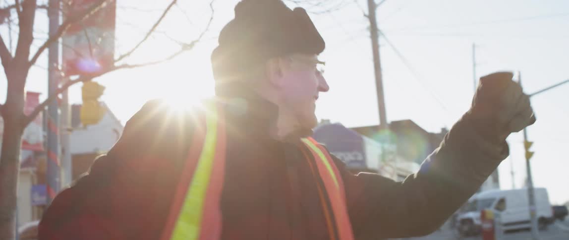 A man wearing a safety vest punches the air and smiles while traffic passes
