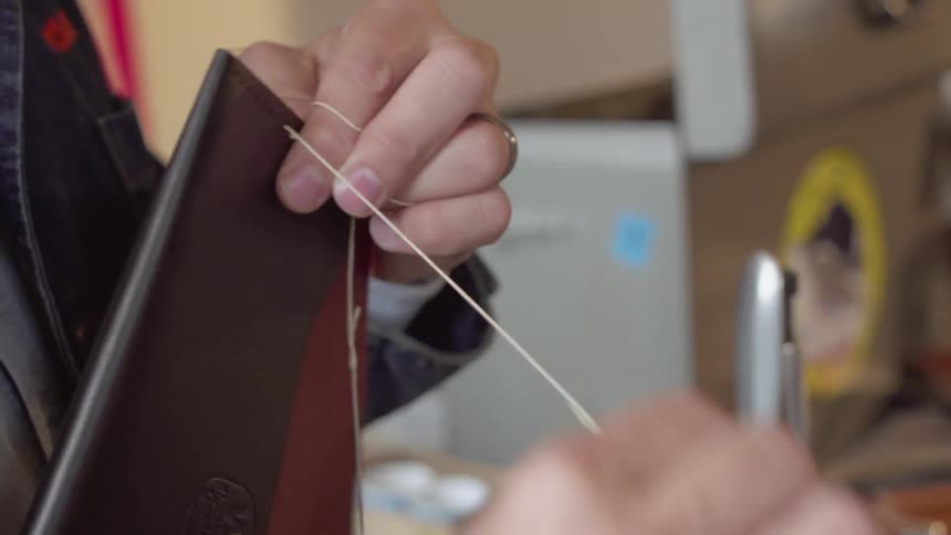 Man is sewing together leather pouch