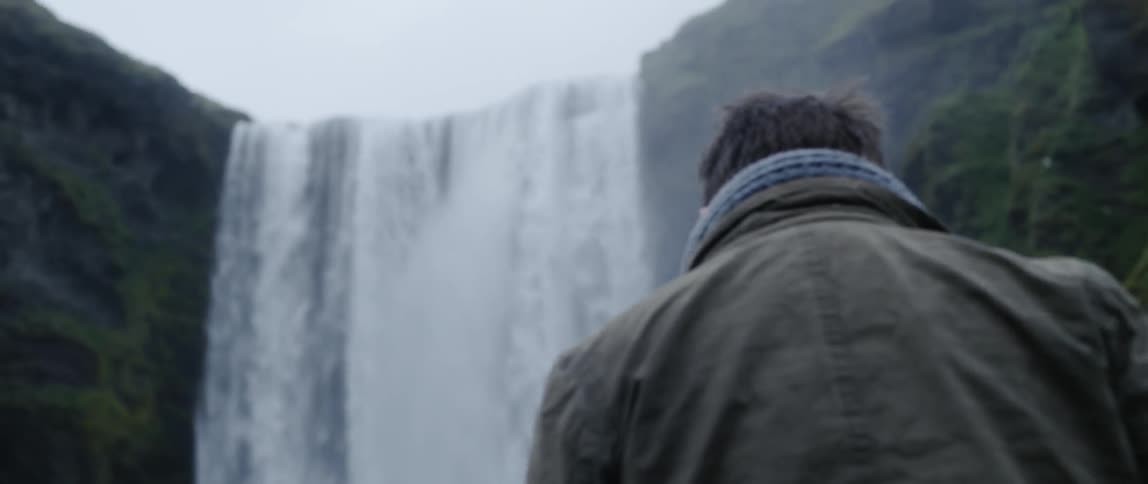 Man is walking toward large waterfall in wilderness