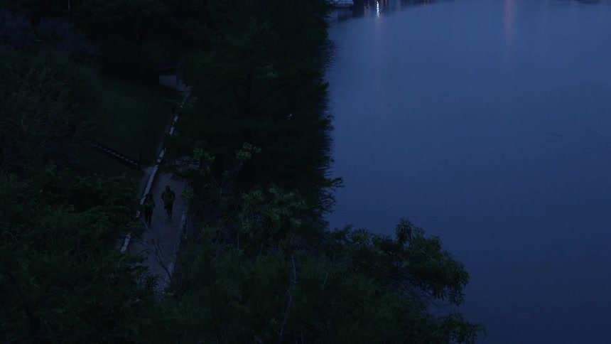 People jog and walk on a path by the water at dusk