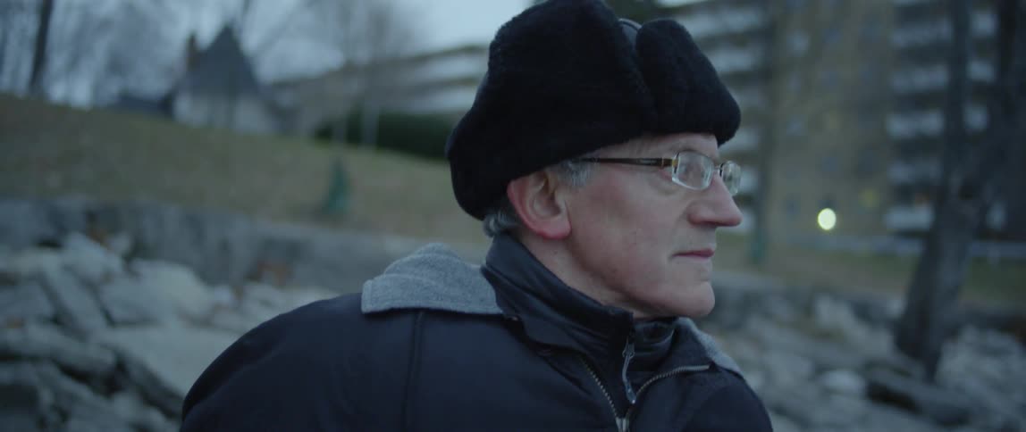 A man wearing a winter hat looks around outside at dusk